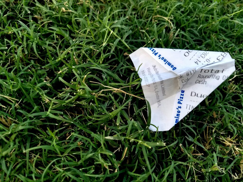 A close-up of a paper plane made from a receipt lying on lush green grass outdoors.